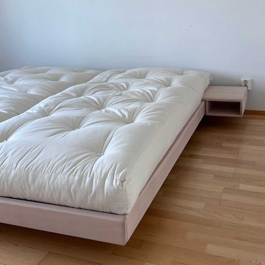 Luonnovalkoinen futonpatja. Kuvassa myös käsittelemättömät Carre sänkyrunko ja Carre yöpöytä.